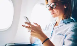Uśmiechnięta kobieta w okularach gra na telefonie, szukając idealnych **grach do samolotu** na długą podróż.