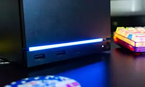 Czarny steam machine z niebieskim podświetleniem, portami USB i gniazdem na kartę SD. Obok kolorowa klawiatura.