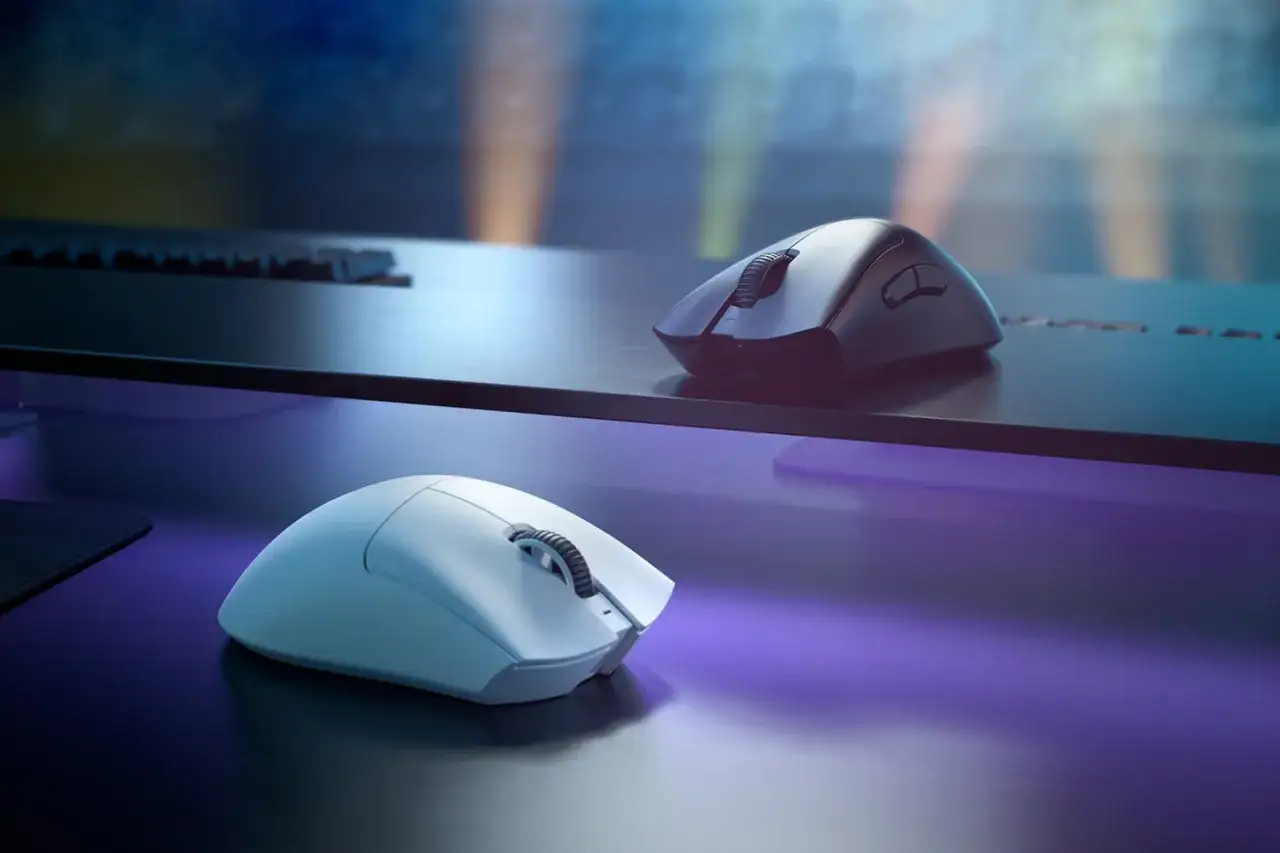 Dwie myszki, biała i czarna, Razer DeathAdder V4 Pro, leżą na biurku w neonowym świetle.